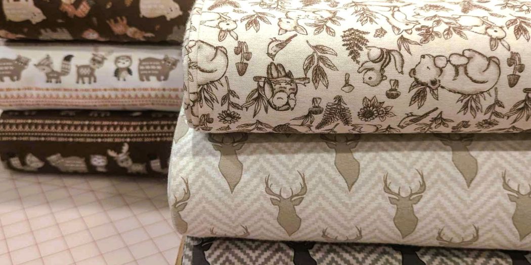 Bolts of printed cotton flannel fabrics featuring woodland animals, deer silhouettes, and whimsical patterns in soft, earthy tones.
