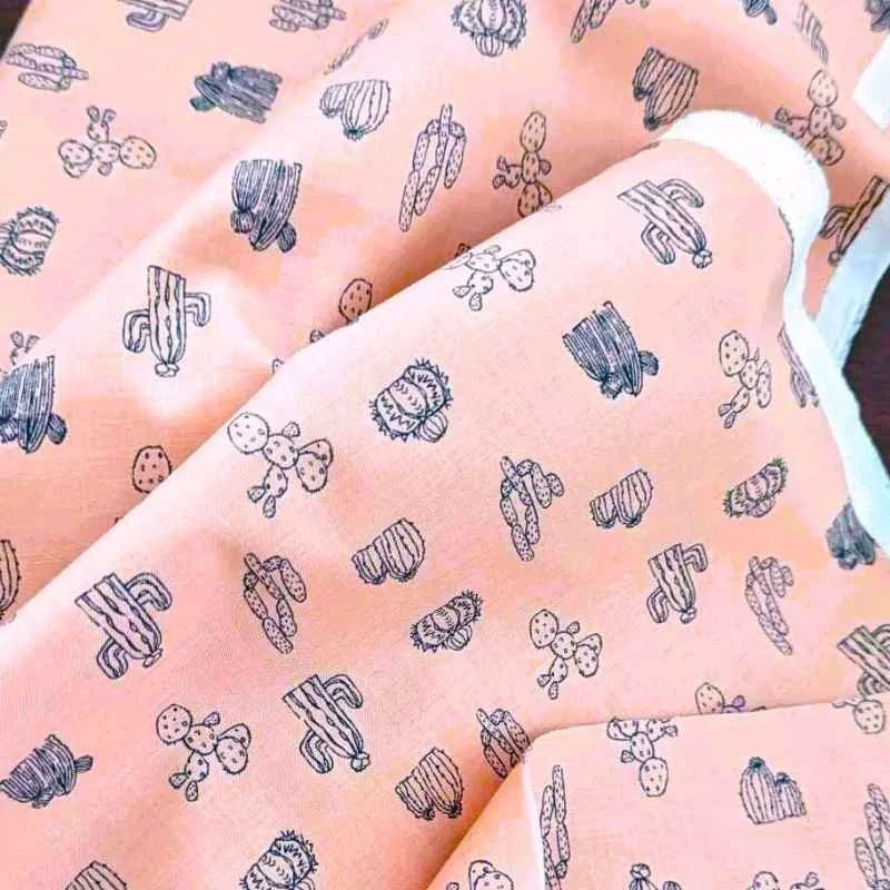 Pink cotton fabric with navy blue cactus line art illustrations.