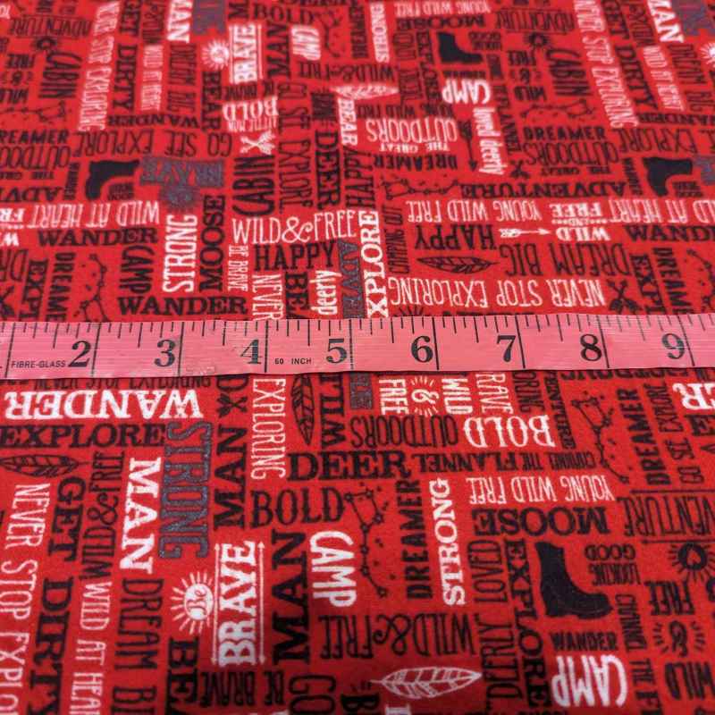 Red cotton flannel with bold white and black adventure-themed text including “Wander,” “Camp,” and “Never Stop Exploring” – 44 inches wide brushed cotton