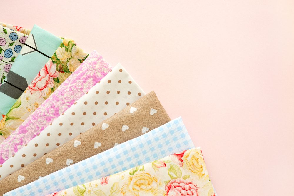 Beyond Quilting: Creative Fabric Projects for Apparel & Home Décor. Natural cotton fabric in the corner of a pink background. Multi-colored cotton fabric for sewing clothes and bedding. Colorful textile and space for text.