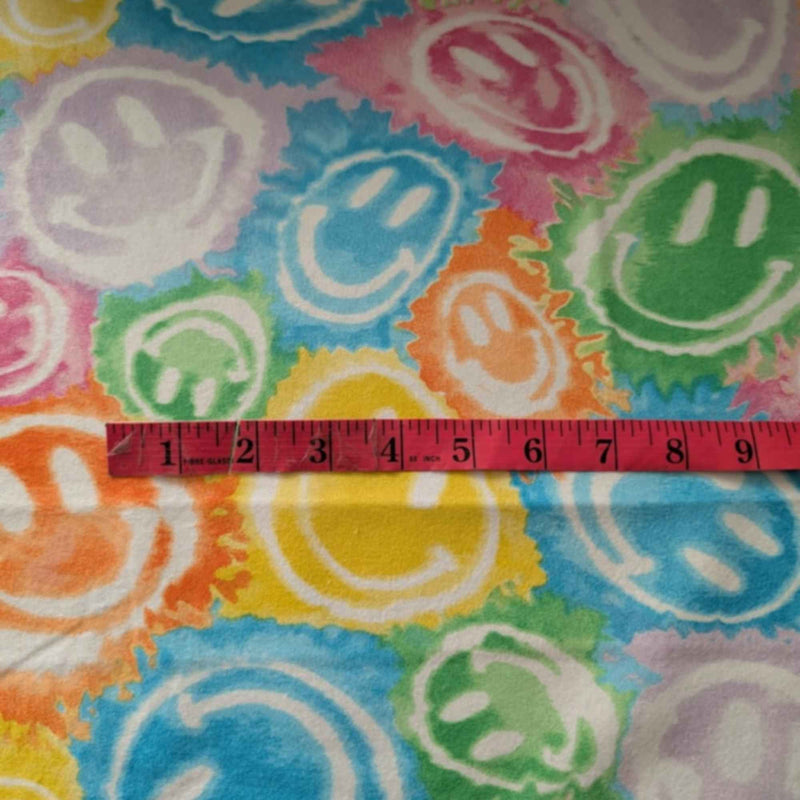 Rainbow smiley faces cotton flannel fabric with colorful tie-dye style print in green, yellow, pink, purple, orange, and blue. Brushed soft, OEKO-TEX certified, 44 inches wide.