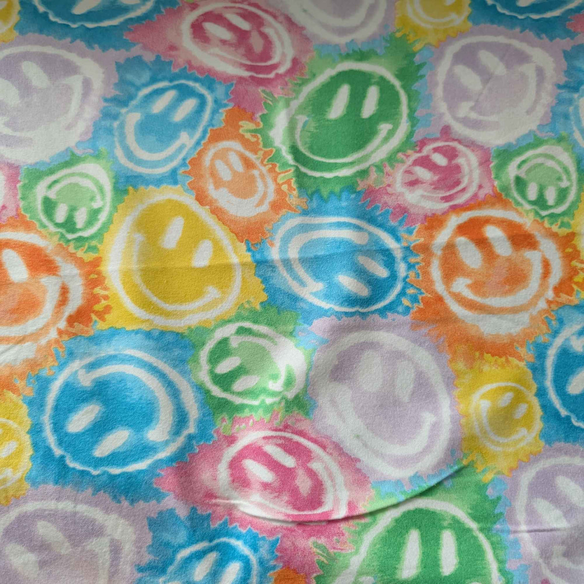Rainbow smiley faces cotton flannel fabric with colorful tie-dye style print in green, yellow, pink, purple, orange, and blue. Brushed soft, OEKO-TEX certified, 44 inches wide.