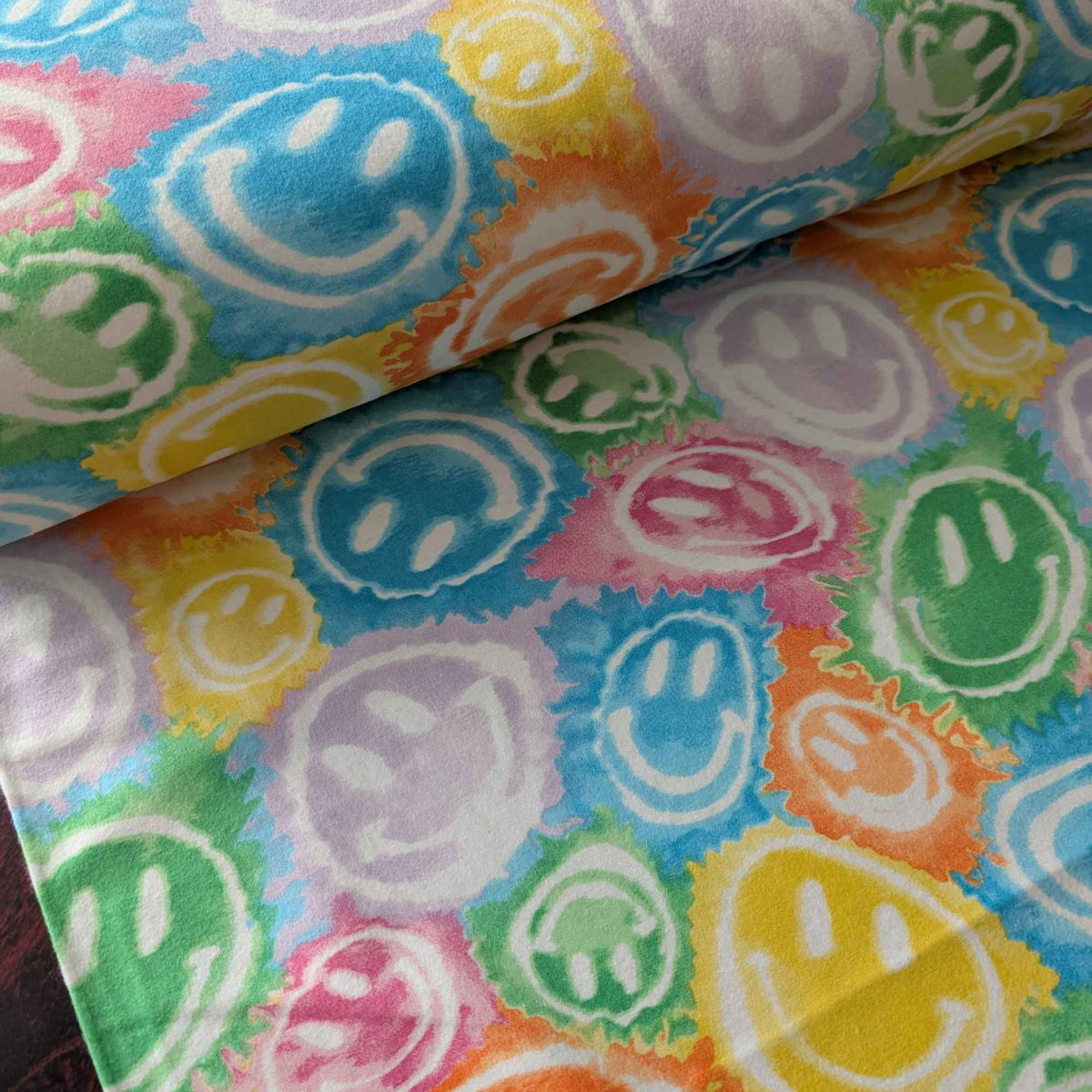 Rainbow smiley faces cotton flannel fabric with colorful tie-dye style print in green, yellow, pink, purple, orange, and blue. Brushed soft, OEKO-TEX certified, 44 inches wide.