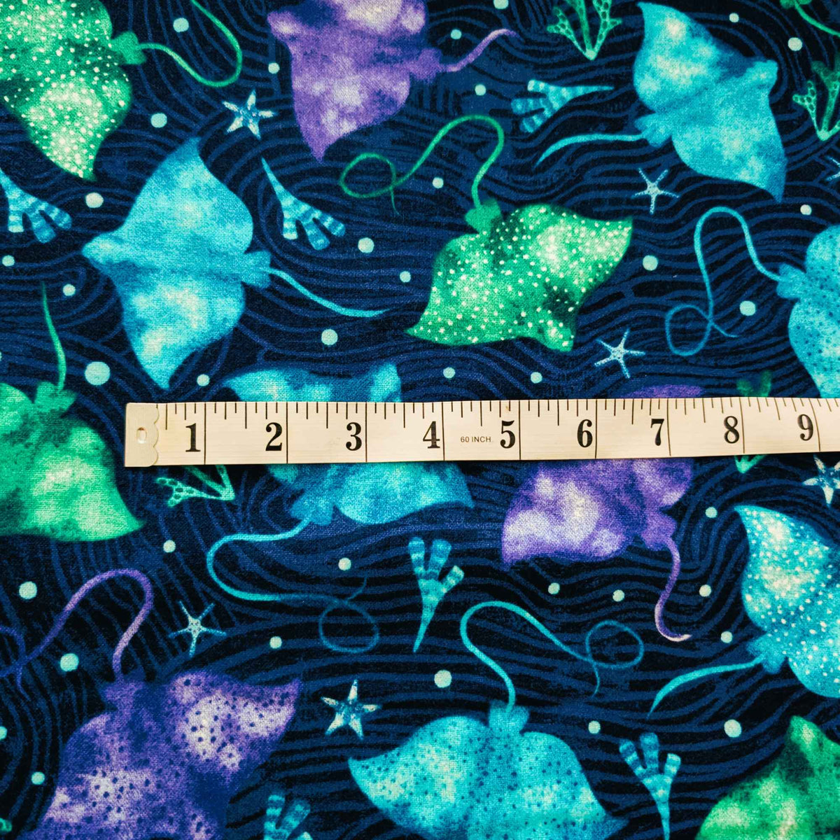 Cotton flannel fabric with colorful stingrays in blue, green, and purple on a dark ocean background with seaweed and starfish. Brushed soft, OEKO-TEX certified, 44 inches wide.
