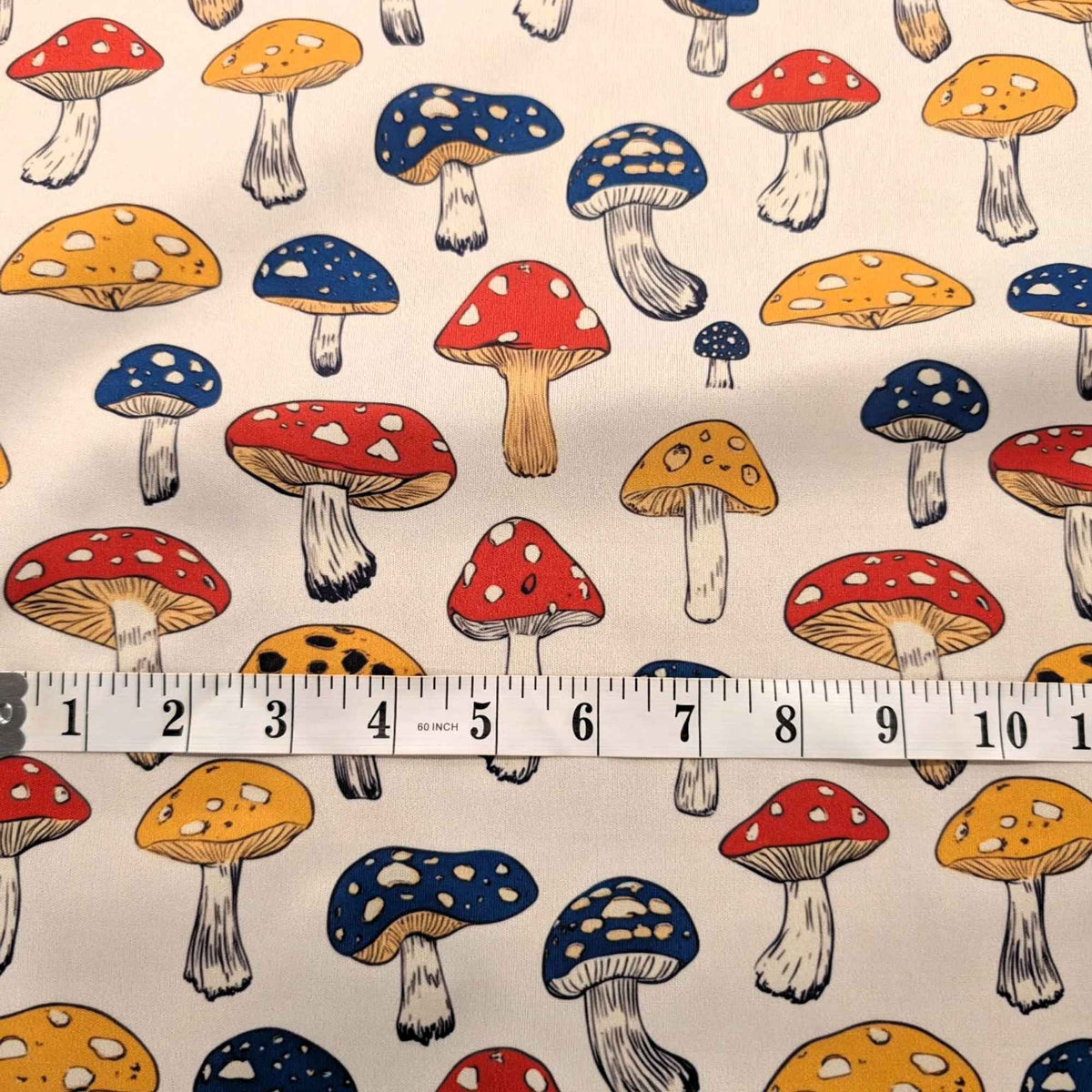 Red yellow and blue mushroom print food safe waterproof PUL fabric on neutral background, 60 inch wide polyester laminate.