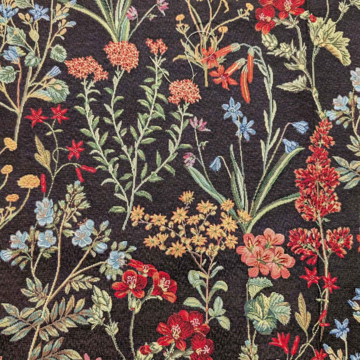 Botanical wildflower Gobelin tapestry fabric with red, coral, blue and yellow flowers and sage green leafy stems on a black background.