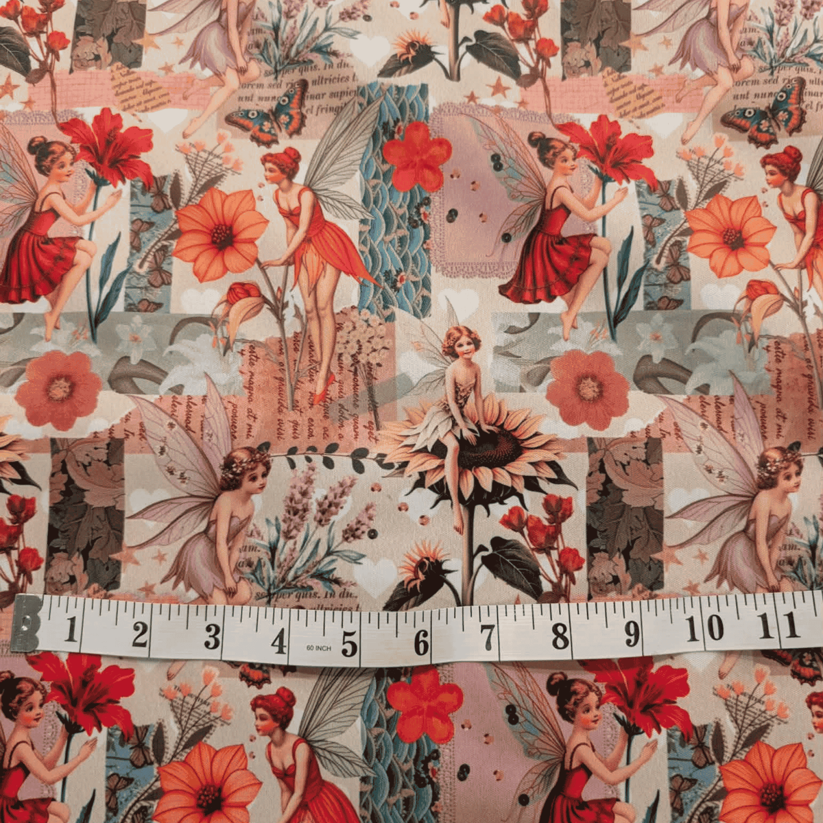 A close-up of patterned fabric featuring vintage-style fairy illustrations, flowers, butterflies, and patchwork panels, with a measuring tape laid across the bottom to show scale.