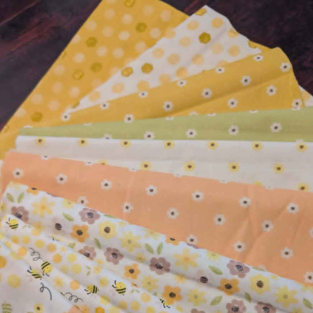 Honey Bear fabric bundle by Camelot Fabrics featuring 10 coordinating quilting cotton prints with bees, florals, daisies, polka dots, honeycomb patterns, and honey bear designs in yellow, peach, cream, and sage green colors