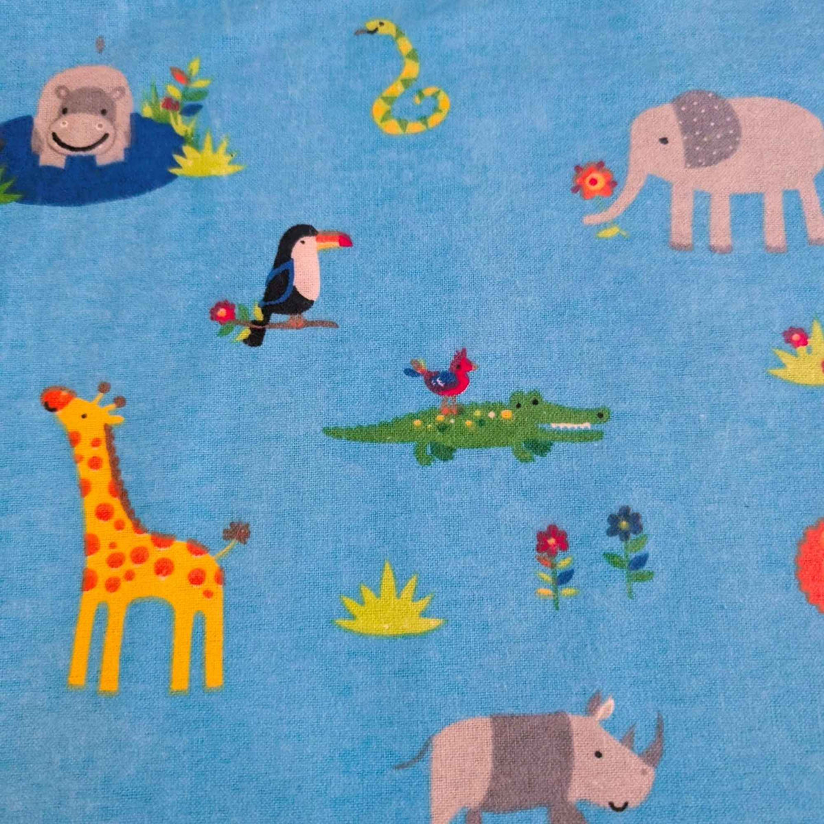 A close-up of a blue fabric with a colorful cartoon safari animal print, featuring a giraffe, elephant, rhinoceros, toucan, crocodile, snake, hippo, and flowers.