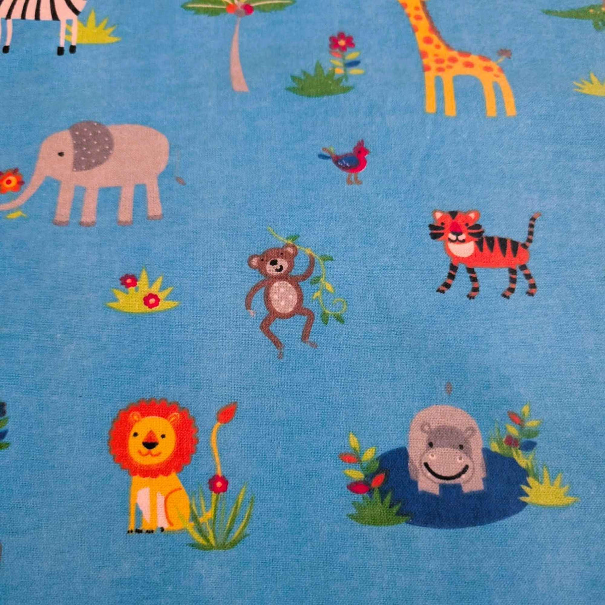 A close-up of a blue fabric featuring a colorful cartoon safari animal print with an elephant, giraffe, zebra, monkey, tiger, lion, hippo, and birds.