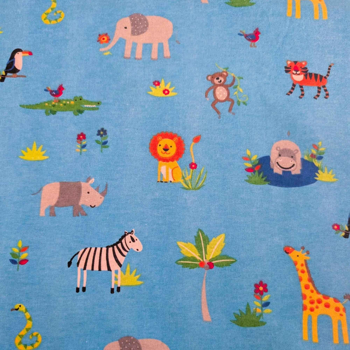 A close-up of blue fabric with a colorful safari animal print, featuring cartoon-style illustrations of a lion, elephant, zebra, giraffe, tiger, crocodile, monkey, rhinoceros, hippo, toucan, and palm tree.