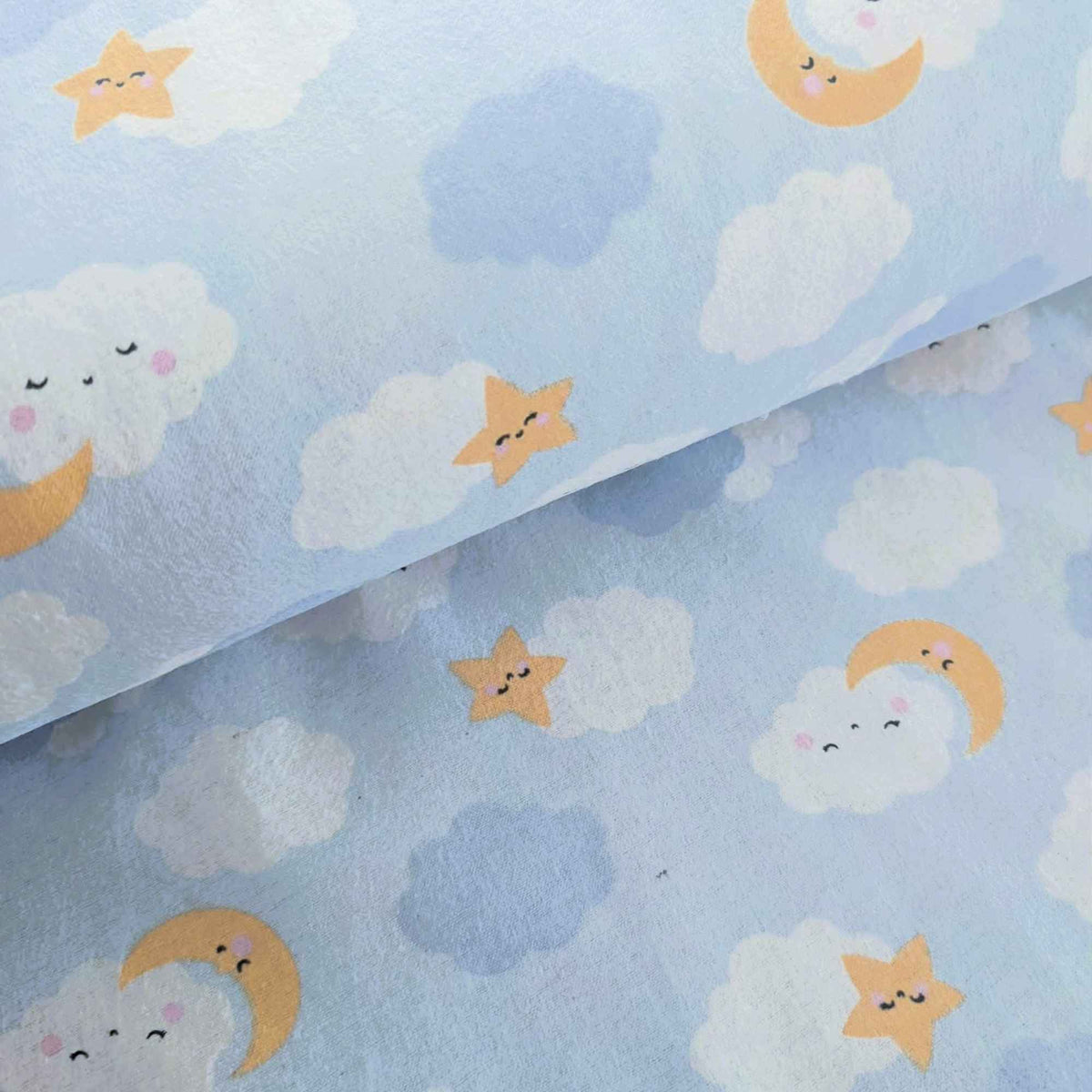 Light blue fabric with a playful celestial print featuring smiling clouds, crescent moons, and stars in soft yellow, white, and light blue.