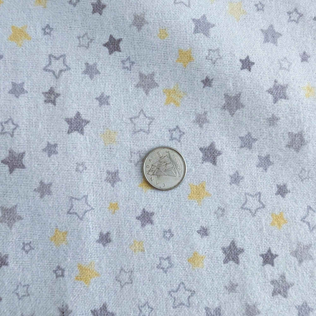 Light blue fabric with a pattern of small stars in lavender and yellow, shown with a silver coin for scale.