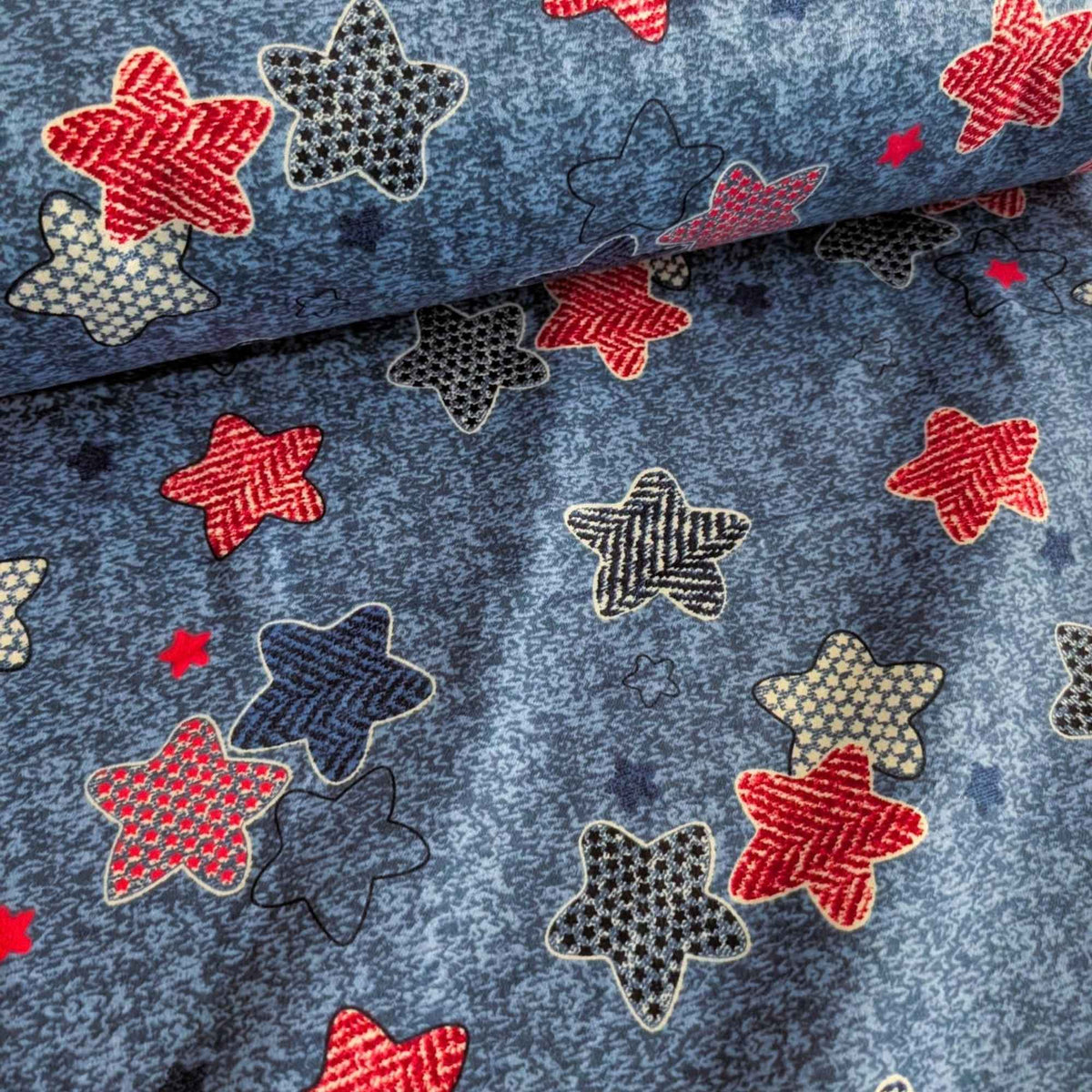 Star print cotton flannel with red, navy, black and cream patterned stars on a textured denim-look blue background.