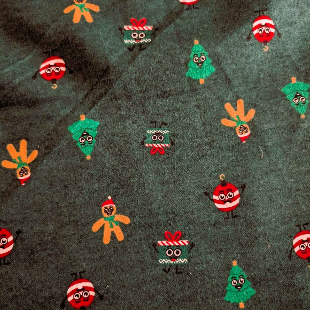 Dark green cotton flannel with smiling Christmas trees, gingerbread figures, red and white ornaments, and gift boxes