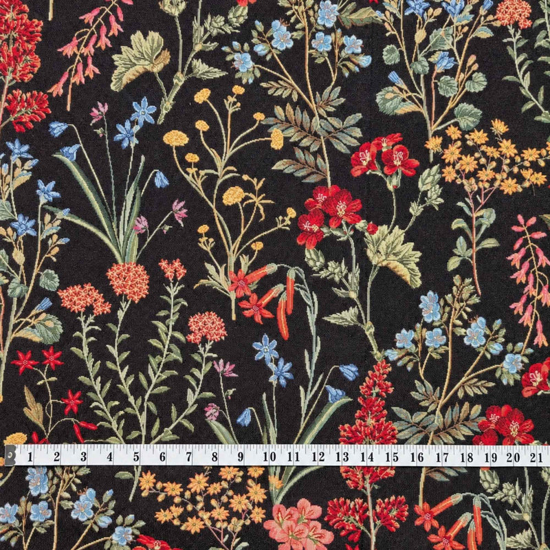 Botanical wildflower Gobelin tapestry fabric with red, coral, blue and yellow flowers and sage green leafy stems on a black background.