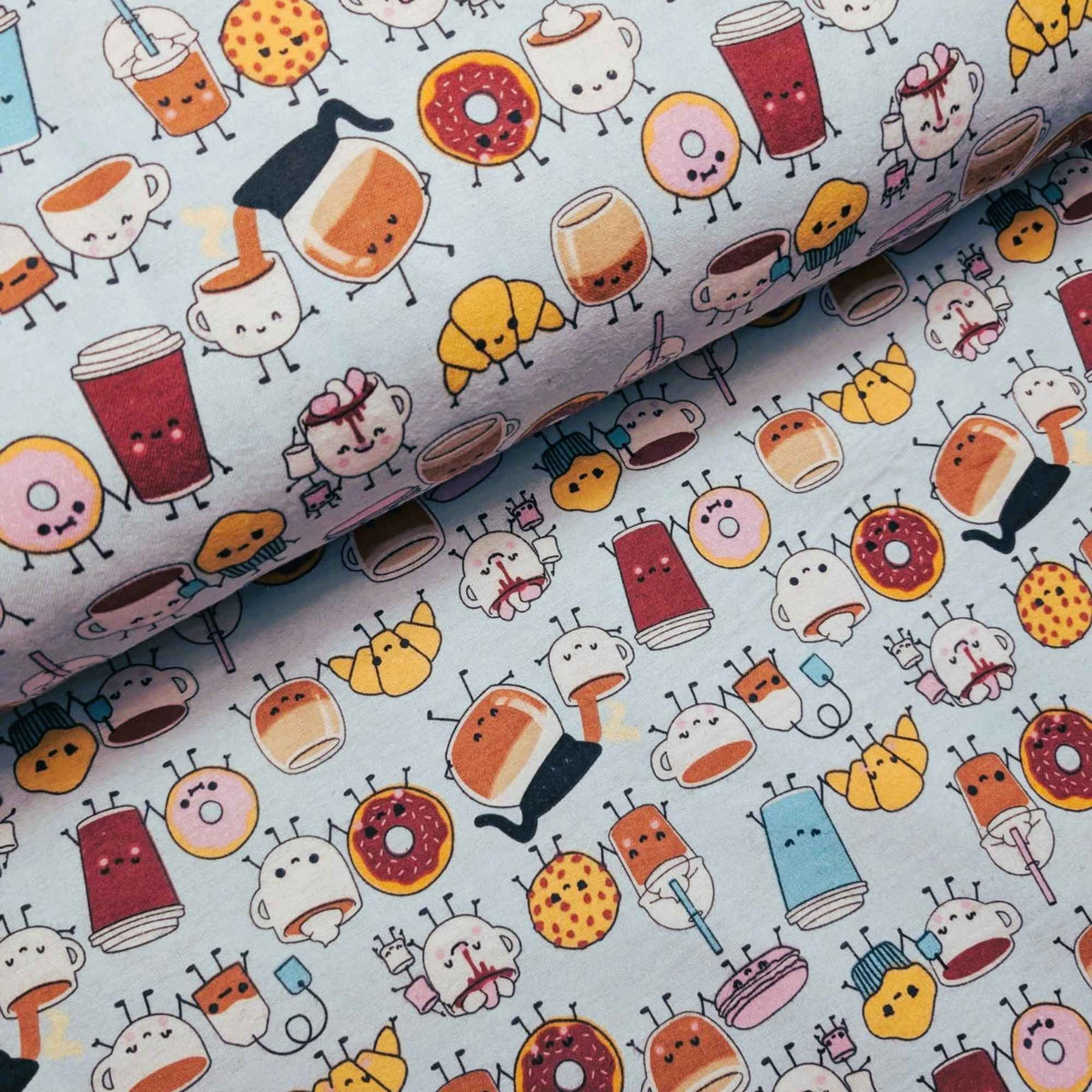 A close-up of a mint green fabric with a repeating cartoon pattern of anthropomorphic donuts, coffee cups, pastries, and small characters in warm colors like orange, yellow, red, pink, and blue.