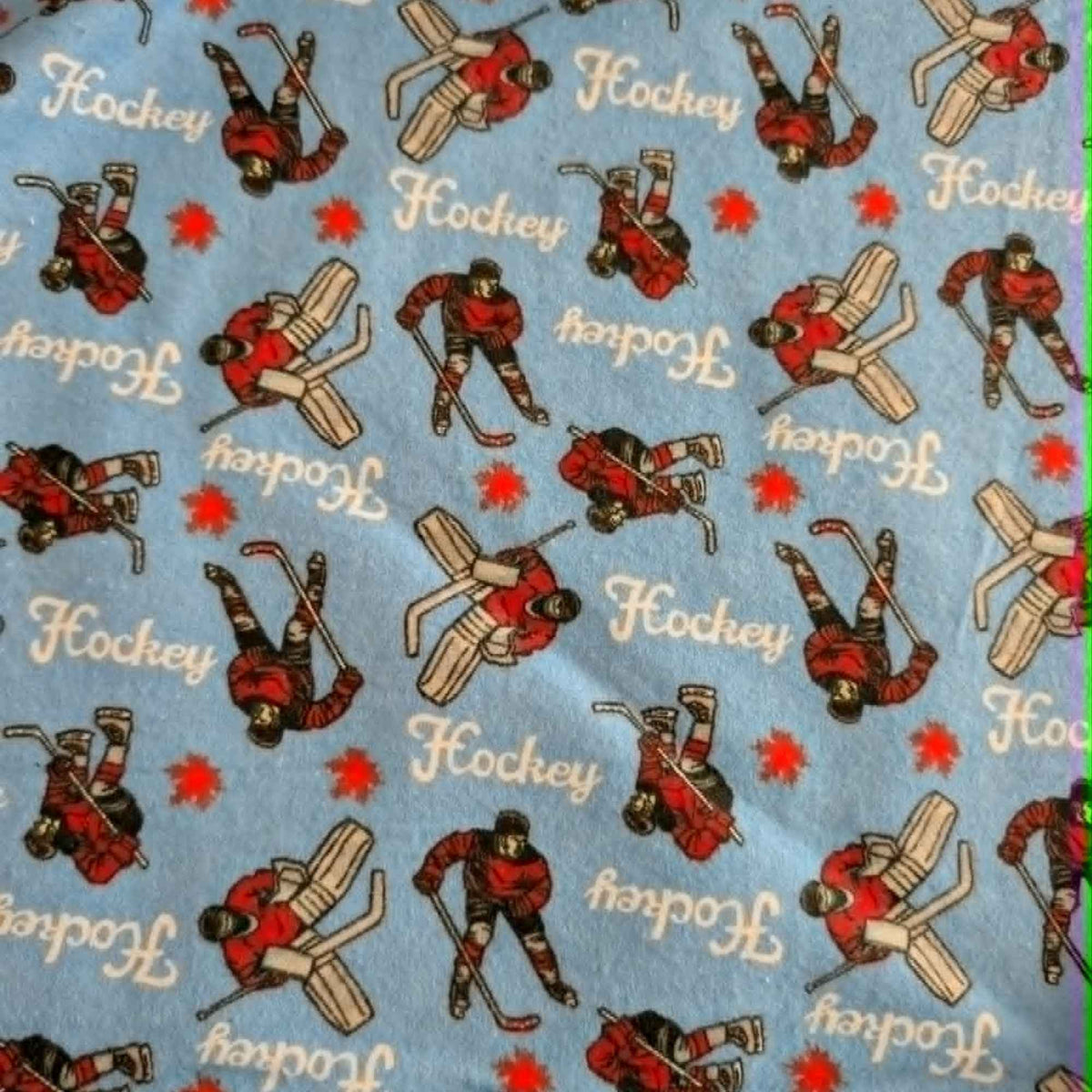 Blue hockey cotton flannel fabric featuring hockey players, goalies, hockey sticks, and hockey text on a soft brushed cotton background.