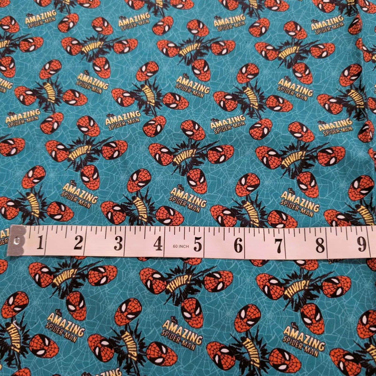 Marvel Amazing Spider-Man quilting cotton fabric by Camelot Fabrics featuring Spider-Man masks, Amazing Spider-Man logos, and comic-style Whip graphics on a turquoise web-pattern background.