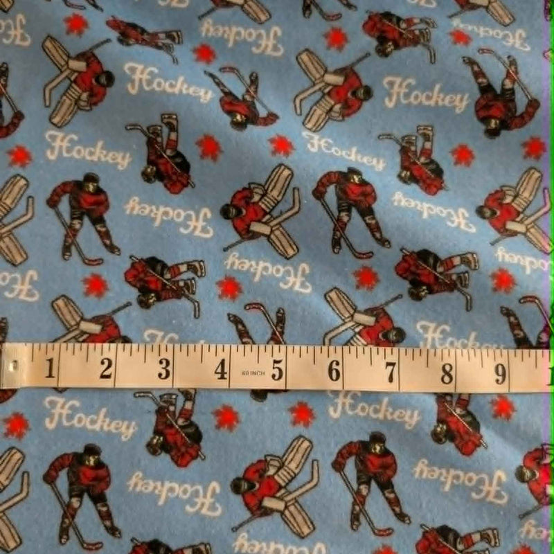 Blue hockey cotton flannel fabric featuring hockey players, goalies, hockey sticks, and hockey text on a soft brushed cotton background.