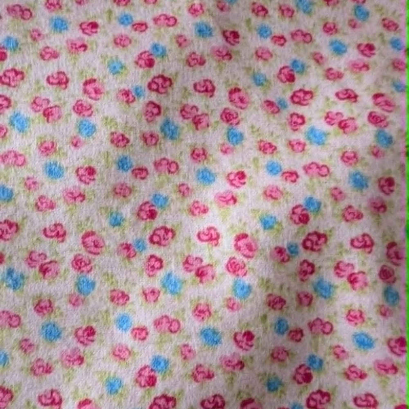 Double brushed flannel fabric featuring tiny pink rosebuds, soft blue flowers, and green foliage scattered across a pink background.