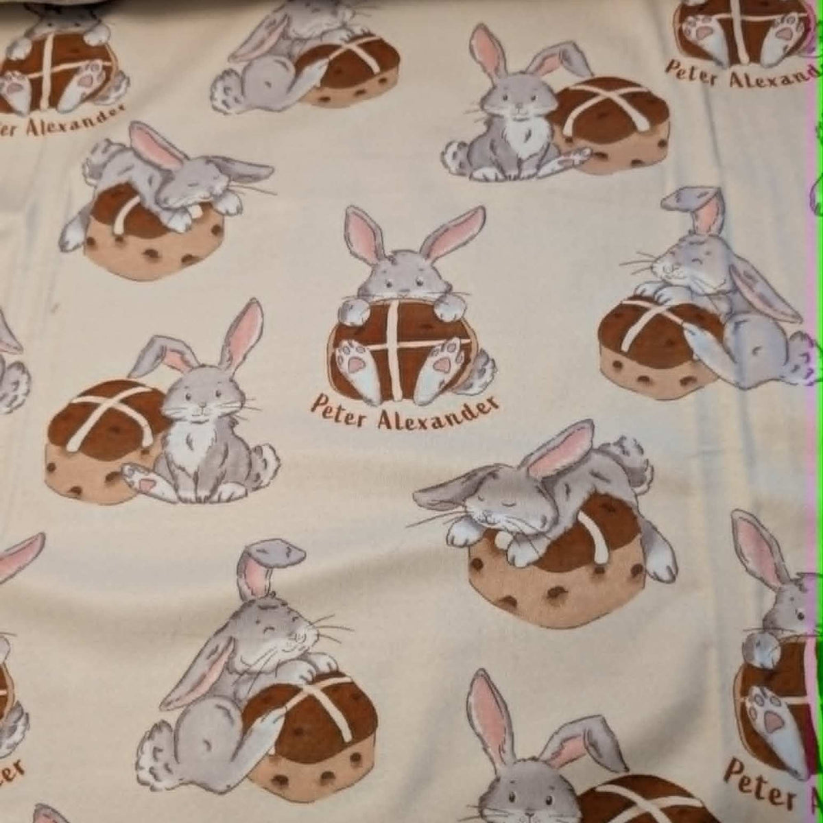 Double brushed flannel fabric featuring adorable bunny rabbits resting beside hot cross buns on a cream background.