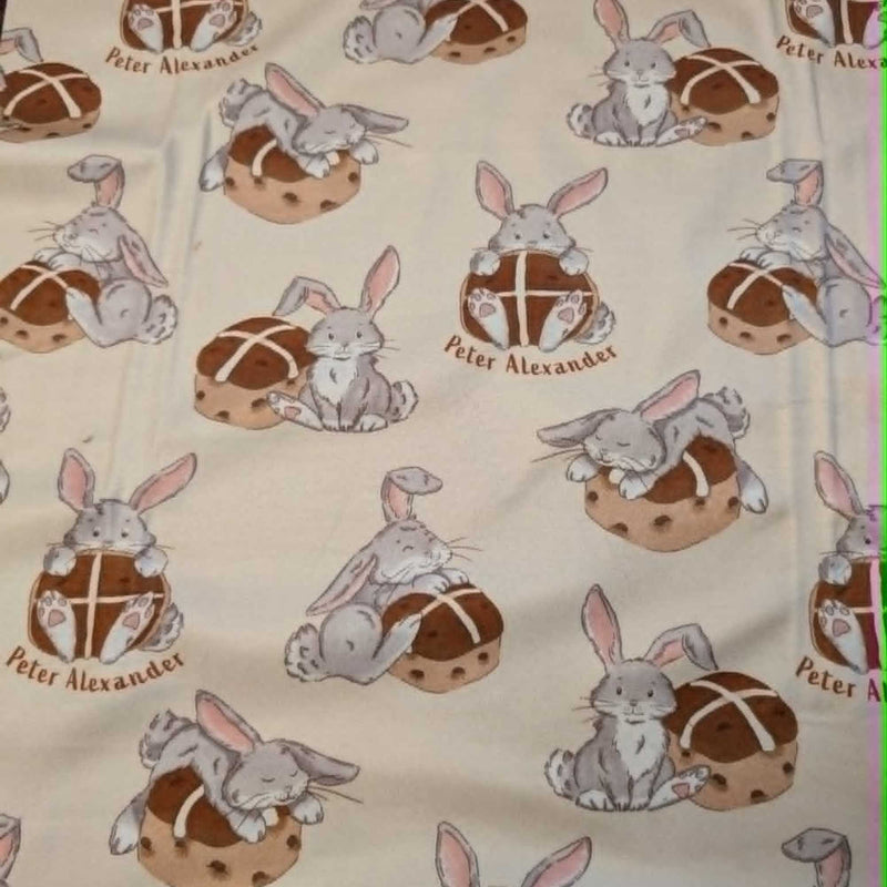 Double brushed flannel fabric featuring adorable bunny rabbits resting beside hot cross buns on a cream background.