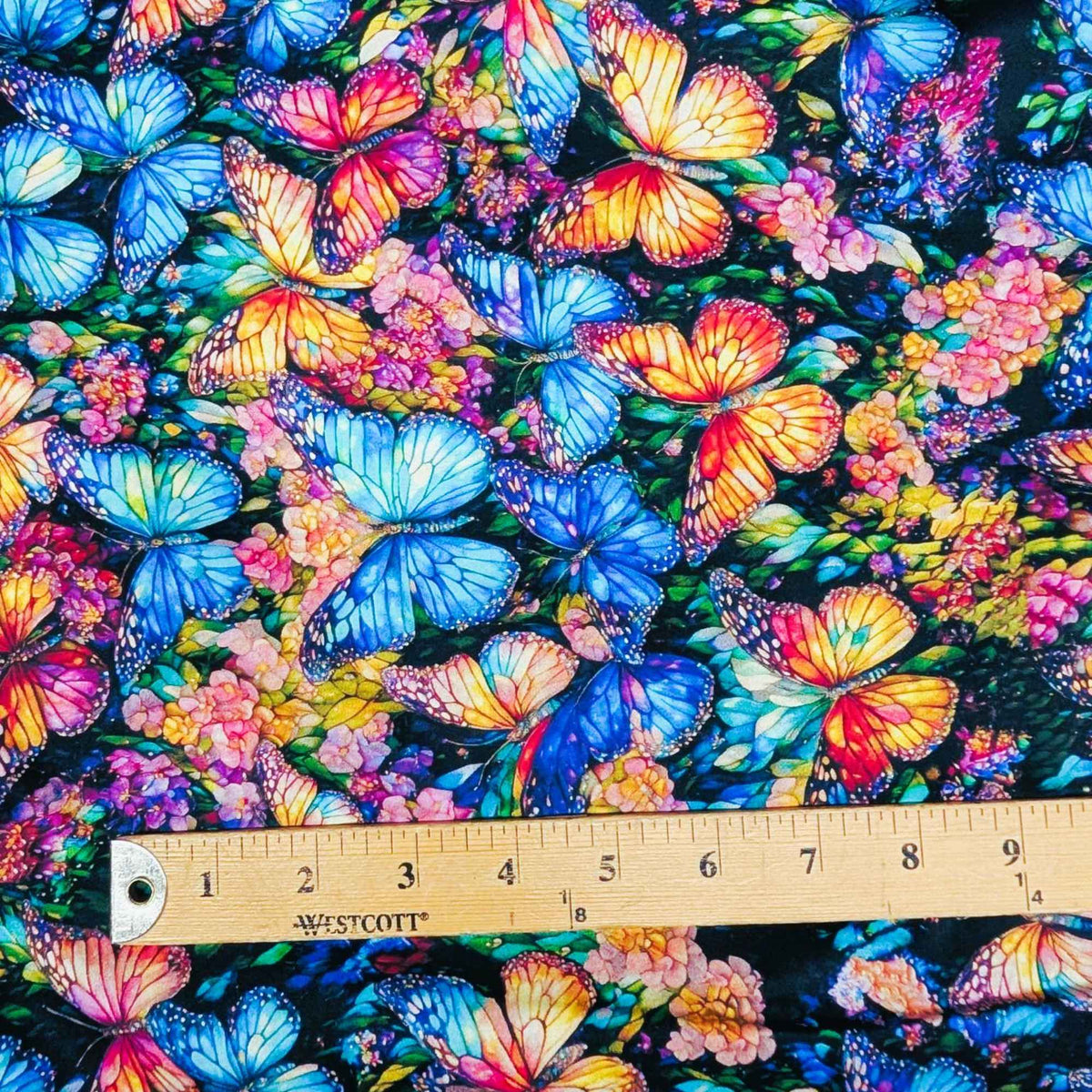 Stained glass butterfly fabric with vibrant blue, orange, and multicolored butterflies on a floral background – Gigi in the Garden 60-inch wide cotton backing